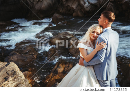 Amazing wedding couple, bride and groom holding hands on a mountains and rivers background. Cute 54178855