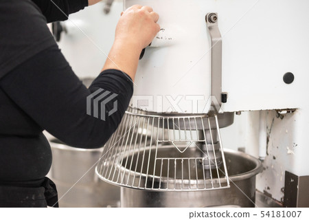 Confectionery factory worker standing and operating industrial dough mixer machine. 54181007