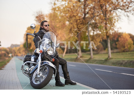 Bearded biker in black leather jacket on modern motorcycle on country roadside. 54193523