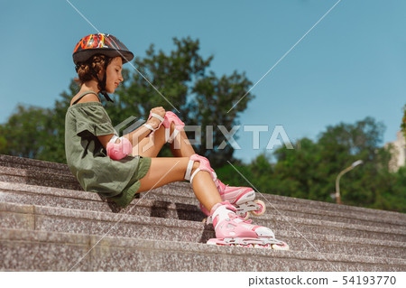 Teenage girl in a helmet learns to ride on roller skates outdoors Teenage girl in a helmet learns to ride on roller skates outdoors 54193770