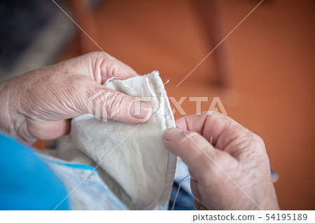 an elderly woman sews torn clothes. close-up of women's hands with thread and needle. the concept of an elderly woman sews torn clothes. close-up of women's hands with thread and needle. the concept of 54195189