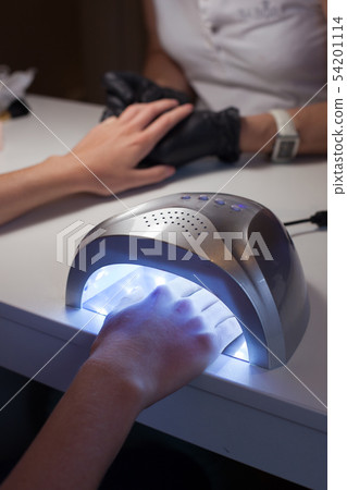 Girl dries nail Polish in a UV lamp. Girl dries nail Polish in a UV lamp. 54201114