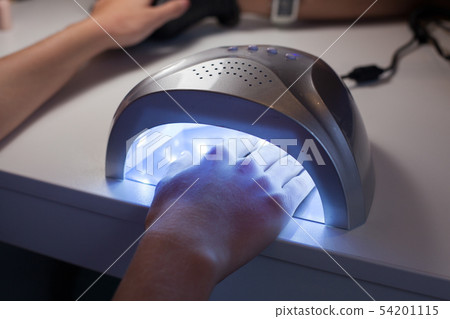 Girl dries nail Polish in a UV lamp. 54201115