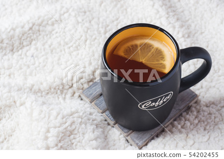 Black mug with tea and lemon on warm soft blanket 54202455