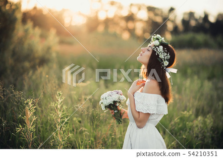 beautiful young girl with a bouquet of flowers and a wreath in a white dress 54210351