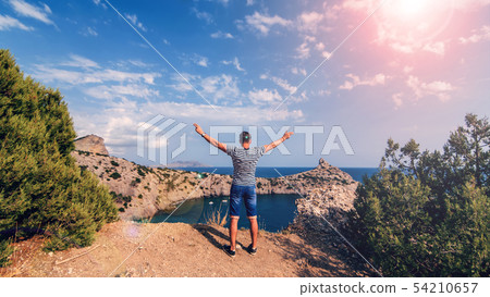 man traveler backs on top of mountains with his hands up against the sea and Sunny sky in summer 54210657