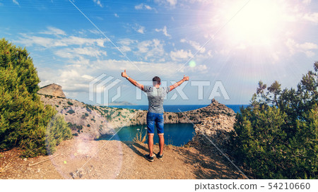 Man with hands raised outdoors in summer on the background of the sea on the top of the mountains 54210660