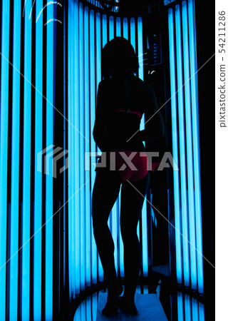 girl in the vertical Solarium. Silhouette on the background of ultraviolet lamps girl in the vertical Solarium. Silhouette on the background of ultraviolet lamps 54211286