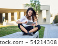 Young woman using digital tablet sitting outdoors 54214308
