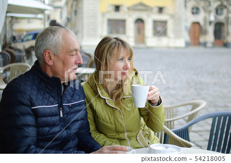 Middle-aged woman and her elderly husband spending time together outdoors sitting in cafe with 54218005