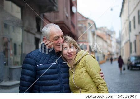 Handsome elderly man is embracing his young blonde wife spending time together outdoors in the Handsome elderly man is embracing his young blonde wife spending time together outdoors in the 54218007