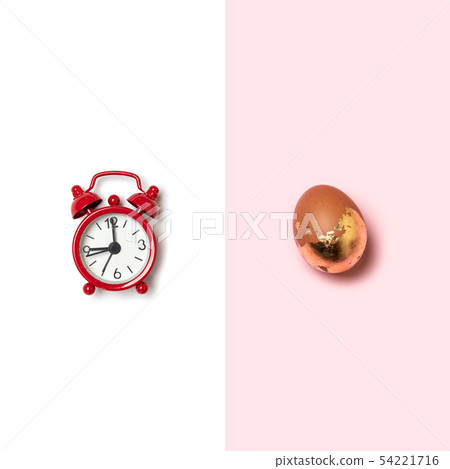 Top view of easter gold egg with red alarm clock on white background Top view of easter gold egg with red alarm clock on white background 54221716