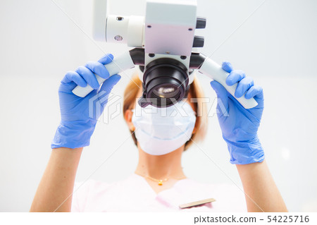 A female dentist is looking into a dental microsco 54225716