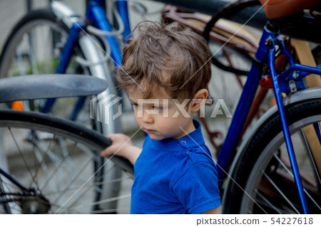 toddler boy plays enthusiastically with big bikes on a city bike parking 54227618