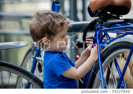 toddler boy plays enthusiastically with big bikes on a city bike parking 54227648