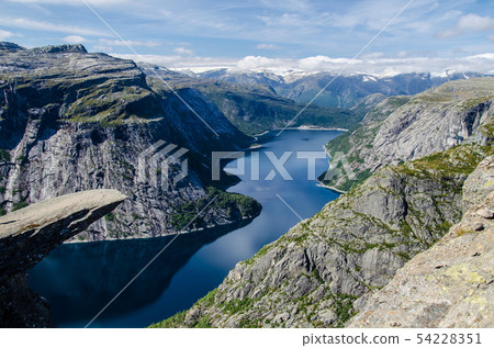 Spectacular view of Trolltunga rock with a blue lake 700 meters lower and interesting sky with few Spectacular view of Trolltunga rock with a blue lake 700 meters lower and interesting sky with few 54228351