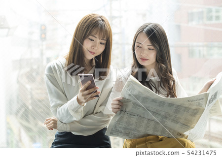 Two women who watch smartphone and newspaper at window side Two women who watch smartphone and newspaper at window side 54231475