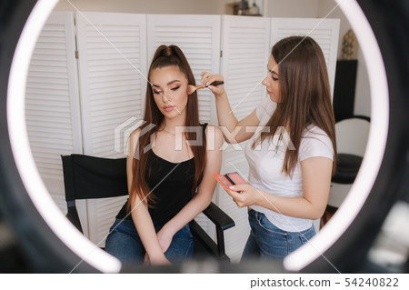 Photo though the ring lamp of makeup artist making a makeup for attractive young girl. Background of 54240822