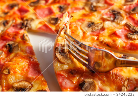 Close up fork takes a piece. Pizza with ham and mushrooms. Delicious hot food sliced and served on 54243222