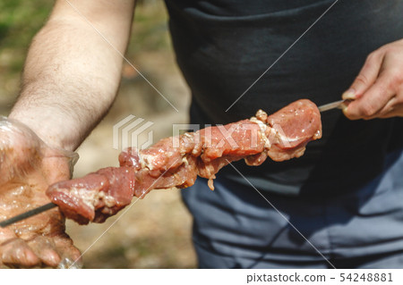 man stringing meat on a skewer. Close-up. 54248881
