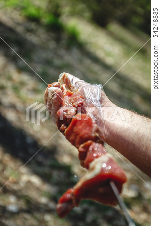 man stringing meat on a skewer. Close-up. 54248885