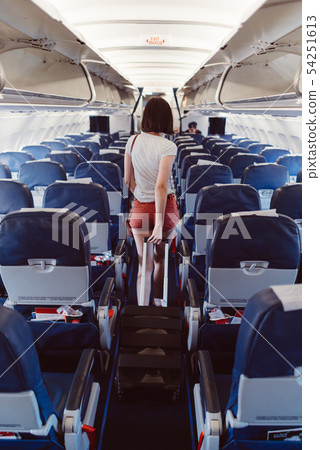 Back view of young woman walking the aisle on plane 54251613