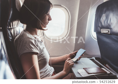 Girl using a smartphone while flying in a plane. 54251629