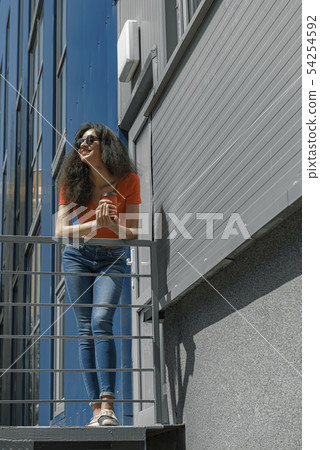 Beautiful young woman with coffee cup leaning on handrail Beautiful young woman with coffee cup leaning on handrail 54254592