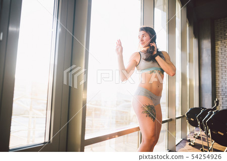 Young caucasian sporty woman with curly long hair poses in sportswear near a panorman window in a 54254926