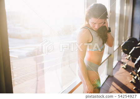 Young caucasian sporty woman with curly long hair poses in sportswear near a panorman window in a 54254927