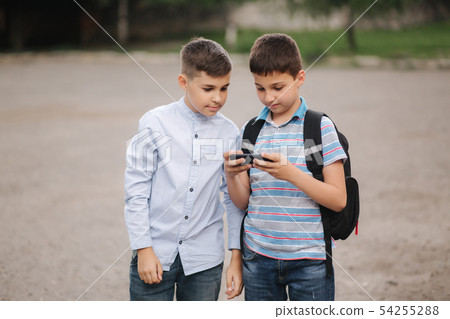 Two boys plays online games after school classes. Young boys smile and use phone Two boys plays online games after school classes. Young boys smile and use phone 54255288