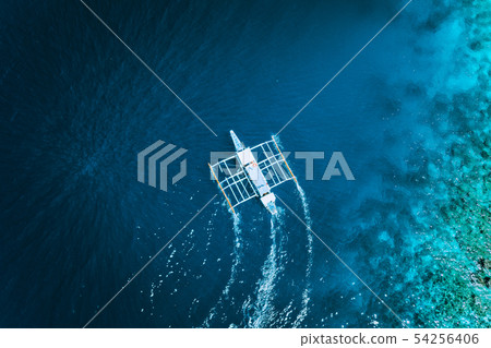 Aerial drone view of white traditional Filipino boat floating on top of clear blue water surface. El 54256406