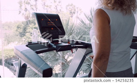 Senior woman is engaged on a treadmill in the gym against the background of the panoramic window.  54258235
