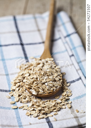 Oat flakes in wooden spoon on linen napkin, golden Oat flakes in wooden spoon on linen napkin, golden 54271507