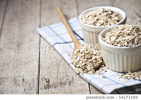 Oat flakes in ceramic bowls and wooden spoon on 54271509