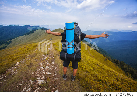 A tourist walks along a mountain meandering trail. Summer walking in mountains A tourist walks along a mountain meandering trail. Summer walking in mountains 54273663
