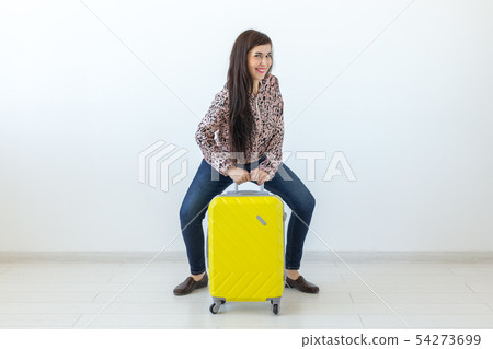 Young woman posing sitting on a yellow suitcase against the background of a white wall with copy Young woman posing sitting on a yellow suitcase against the background of a white wall with copy 54273699