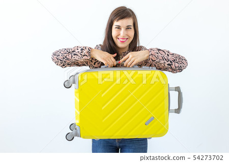 Joyful smiling young brunette woman posing with a yellow suitcase while waiting for a vacation. The Joyful smiling young brunette woman posing with a yellow suitcase while waiting for a vacation. The 54273702