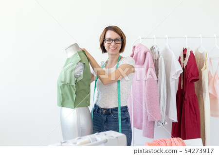 Positive cute smiling young seamstress woman in glasses with a measuring tape making a new garment 54273917