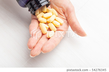 Female hand holds yellow pills on a white table background next to a jar. Concept of treatment of Female hand holds yellow pills on a white table background next to a jar. Concept of treatment of 54276345