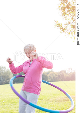 Active senior woman hula hooping in park Active senior woman hula hooping in park 54278923