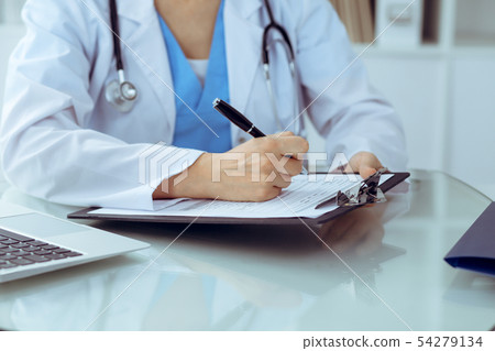 Doctor woman filling up medical form while sitting at the table, close-up of hands 54279134