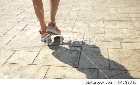 feet close up, pedestrians walk down the street. Girl's legs in pink leather sandals on a white high 54285386