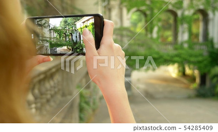 Young woman taking pictures with phone of a colonnade of an old castle 54285409