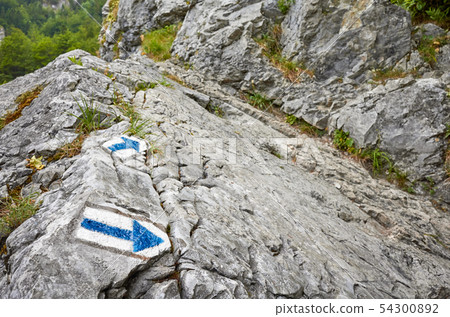 Hiking trail blue paint arrow marking on a rock. Hiking trail blue paint arrow marking on a rock. 54300892
