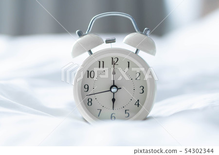 Alarm clock on white bad with light from window 54302344