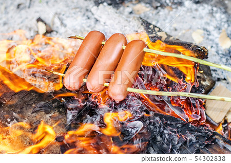 Grilling sausages over an open fire outdoors. Grilling sausages over an open fire outdoors. 54302838