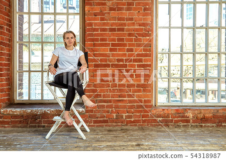 Beautiful cheeky young girl is sitting in a chair by the brick wall. Background brick brick, copy 54318987