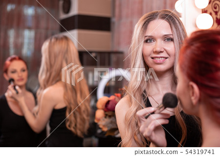 Makeup artist applying liquid tonal foundation on the face of the woman in white make up room 54319741