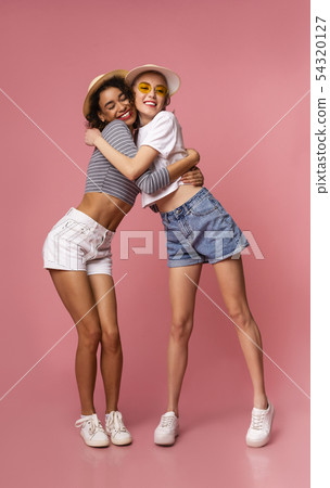 Happy girls in casual summer wear hugging on pink background, full-length photo 54320127